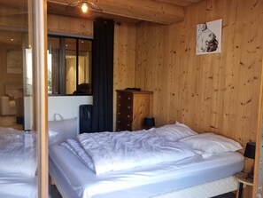 Ein Zimmer mit Holzwänden, einem Bett mit weißer Bettwäsche, einem Spiegel, einer Kommode und einer Lampe.