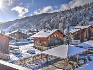 A snow-covered village with wooden buildings, a parking area, and a mountain backdrop. - Cozy apartment near center - 4/6 guests (Morzine)