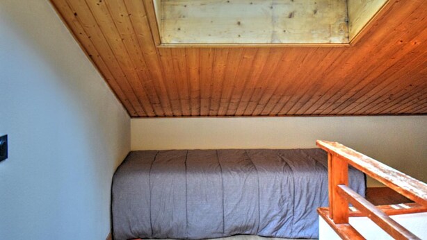 Una habitació amb sostre inclinat, un fanal i un llit amb capçalera de fusta.
