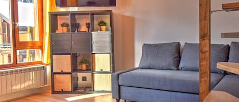 A modern living room with a grey sofa, wooden flooring, and a built-in bookshelf with plants.