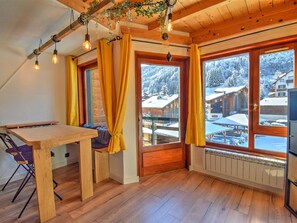 Une pièce avec une table en bois, des chaises, de grandes fenêtres et une vue sur un paysage enneigé.