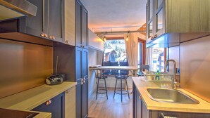Una cuina moderna amb una illa central, tamboretes de bar i vista a un paisatge de muntanya.
