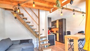 Un interior modern amb una escala de fusta, un sofà gris, una taula de dinar de fusta i una zona de cuina.
