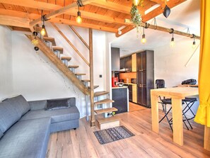 A modern interior with a wooden staircase, a grey sofa, a wooden dining table, and a kitchen area. - Cozy apartment near center - 4/6 guests (Morzine)