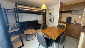 A compact living space with a bunk bed, kitchenette, dining area, and a hanging light fixture. - Studio cabin with mountain view - 4 guests (Les Adrets-Prapoutel)
