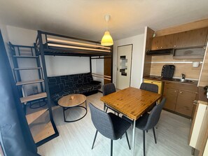 Ein gemütlicher, kompakter Wohnbereich mit Etagenbett, Küchenzeile, Essbereich und einer Pendelleuchte.