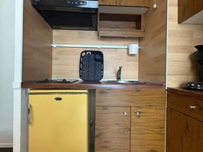 Eine kleine Küche mit integriertem Mikrowellenherd, einem kleinen Kühlschrank und Holzschränken.