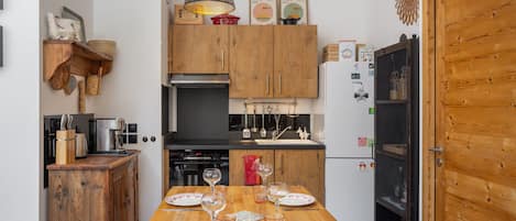A kitchen with wooden cabinets, a dining table set with plates and glasses, and hanging pendant lights.