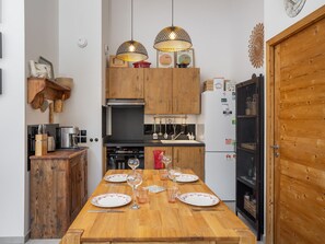 Eine Küche mit Holzausstattung, einem Essplatz mit Tellern und Gläsern sowie hängenden Pendelleuchten.