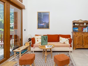 A cozy living room with a sofa, two ottomans, a small table, a bookshelf, and a large window with a view of greenery. - New apartment near village - 4 guests (Le Monêtier-les-Bains)