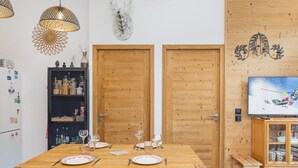 Un coin repas avec une table en bois dressée pour quatre personnes, deux portes, un téléviseur et une étagère avec des bocaux.