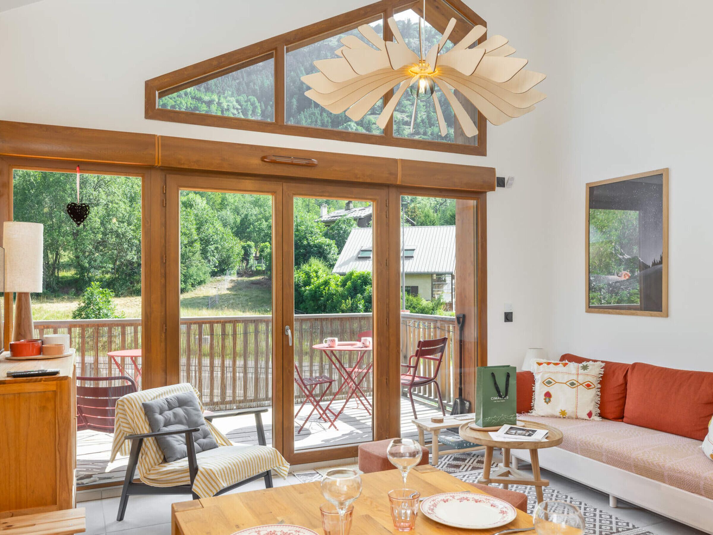 A spacious room with a large sliding glass door leading to a deck, a wooden ceiling, and a modern chandelier.