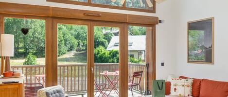 A spacious room with a large sliding glass door leading to a deck, a wooden ceiling, and a modern chandelier.