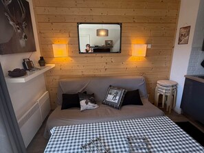 Ein gemütliches Zimmer mit einem Bett, einem Spiegel, zwei Wandleuchten, einem kleinen Tisch und einer Heizung.