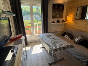 Ein Zimmer mit einem Bett, einem Tisch mit kariertem Tischläufer, einem Fernseher und einem Hirschbild an der Wand.