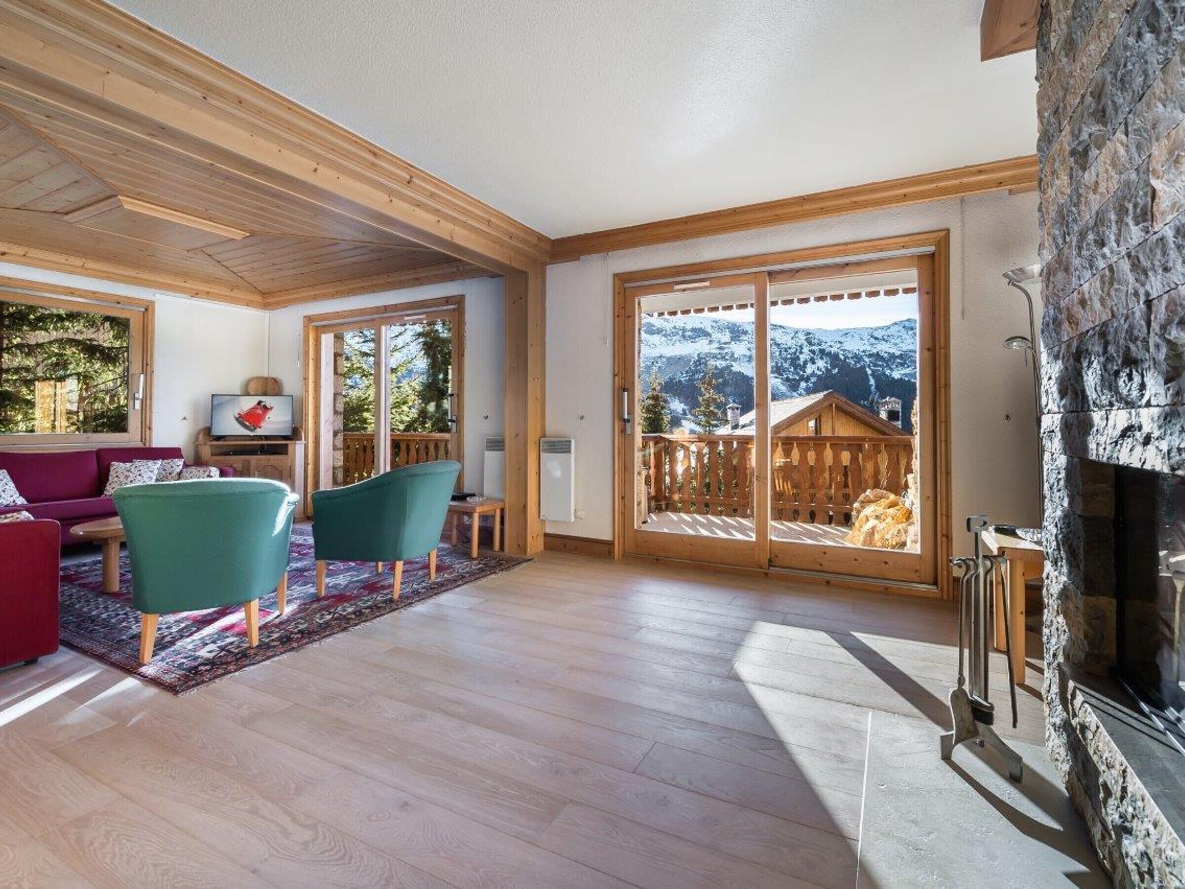 Ein geräumiges Wohnzimmer mit Kamin, Holzboden und einer großen Glasschiebetür, die auf einen Balkon mit Bergblick führt.