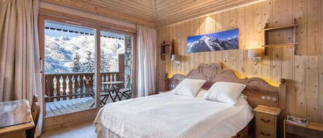 A wooden-paneled bedroom with a bed, bedside tables, a mounted TV, and a balcony with a mountain view.