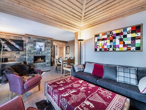 A cozy living room with a fireplace, a stone wall, and a colorful abstract painting. - Spacious apartment pets OK, mountain view - 8 guests (Méribel)
