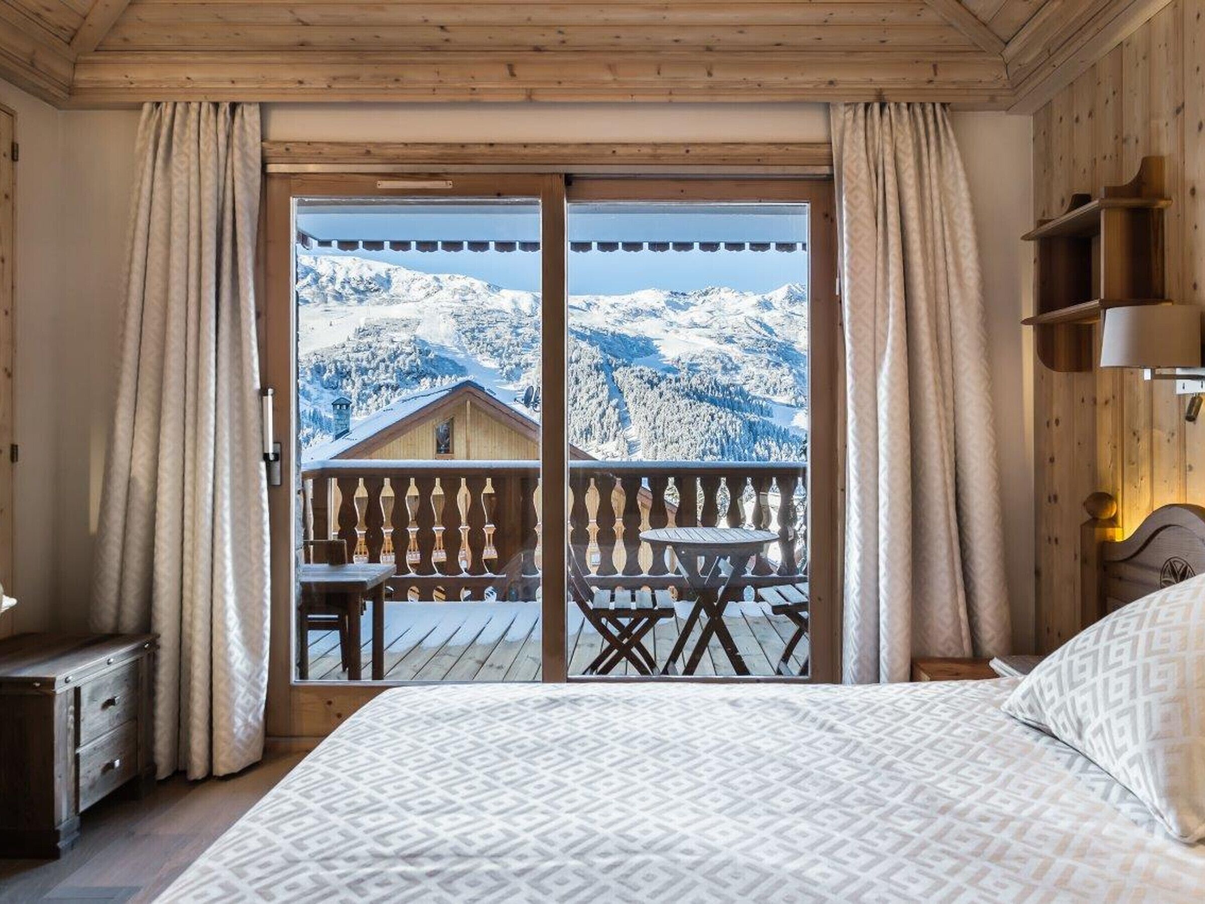 A bedroom with a large bed, wooden headboard, and a view of snow-covered mountains through a balcony.