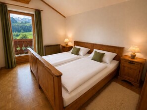 A double bed with a wooden headboard, two bedside tables with lamps, a view of a balcony with curtains, and a radiator.