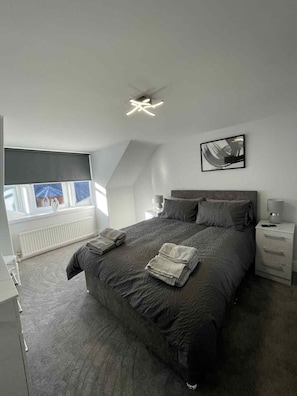 A modern bedroom with a large bed, a bedside table, a nightstand, and a ceiling fan. - Modern Home in Macduff (Aberdeenshire)