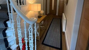 En trappe med hvide gelændere fører op til en platform, en lampe står på et bord, og en dør ses i baggrunden.