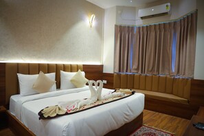 A hotel room with a bed, a headboard, a wall-mounted light, an air conditioning unit, and a window with curtains. - HOTEL RADHA KRISHNAM (Mathura)