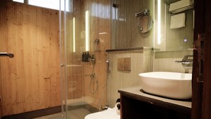 Ett badrum med en duschavdelning med glasväggar, en vit tvättställ och träpanel på väggarna.
