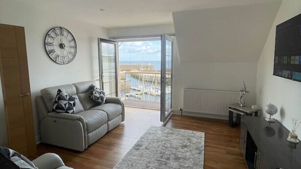 A modern living room with a sofa, a coffee table, and a large window offering a view of a marina.