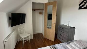 A bedroom with a bed, a chair, a dresser, a television, and a wardrobe.