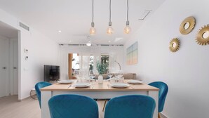 A modern dining area with a wooden table set for four, blue chairs, and pendant lights. - Sotogrande Beach Apartment (San Roque)