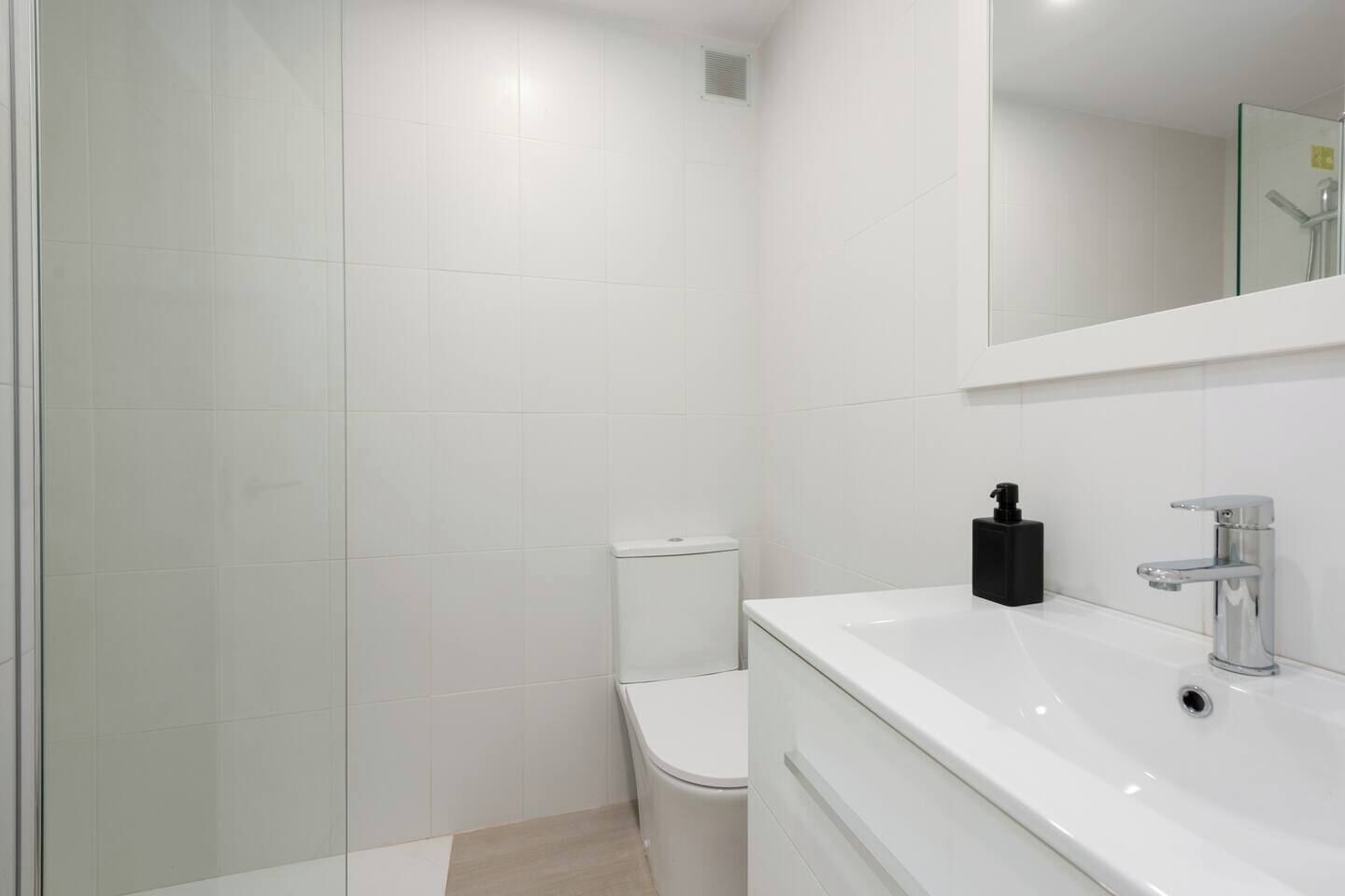 A modern bathroom with a glass shower enclosure, a white toilet, and a white sink with a mirror above.