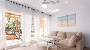 A modern living room with a sofa, a coffee table, and a balcony with outdoor furniture. - Sotogrande Beach Apartment (San Roque)