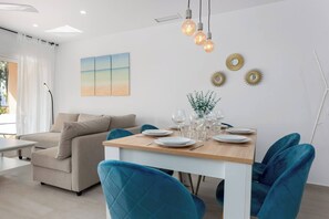 A modern dining area with a wooden table set for four, blue chairs, and a sofa in the background.