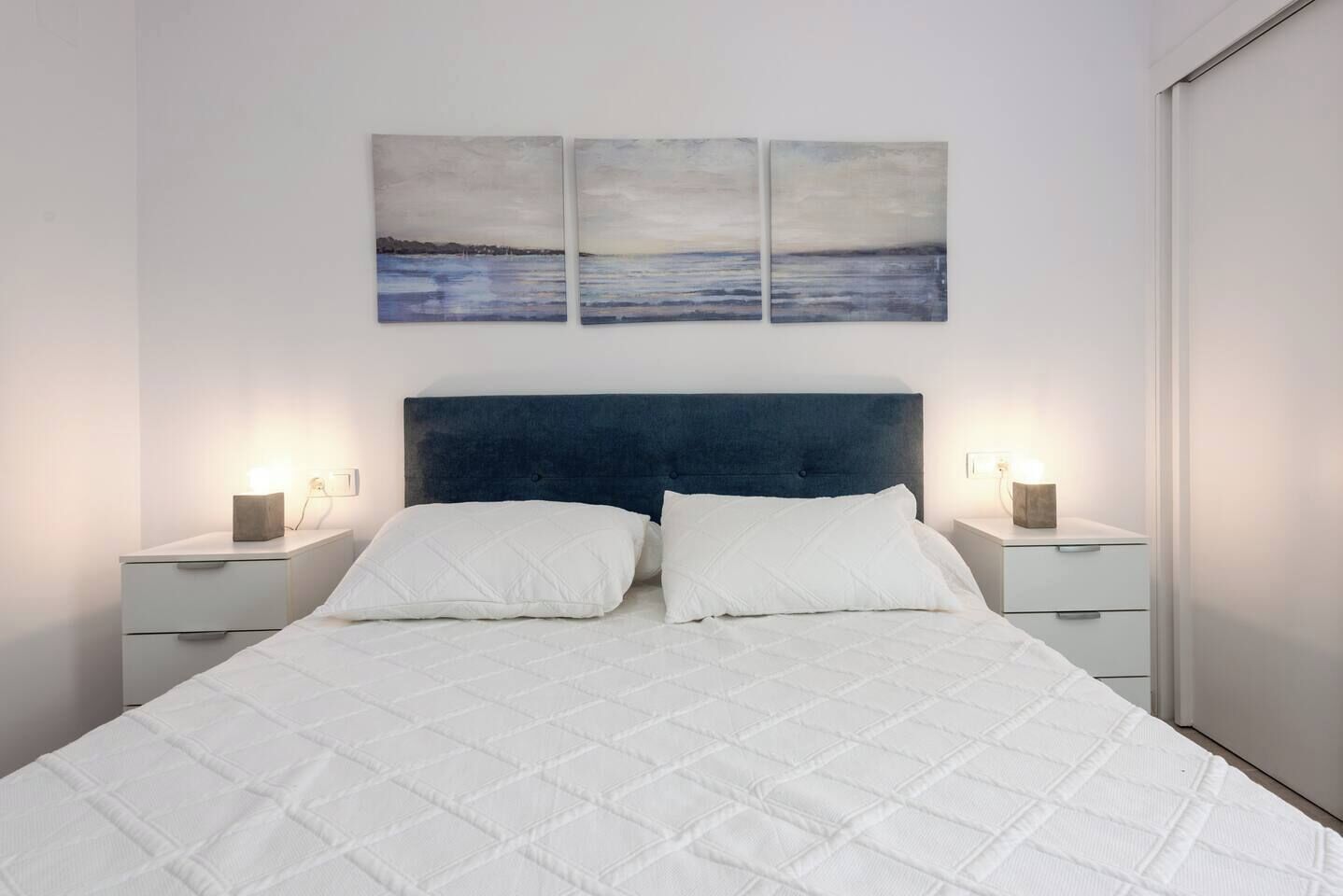 A bedroom with a large bed, two bedside tables, and three wall-mounted paintings.