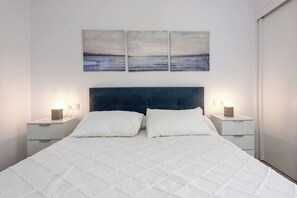 A bedroom with a large bed, two bedside tables, and three wall-mounted paintings.