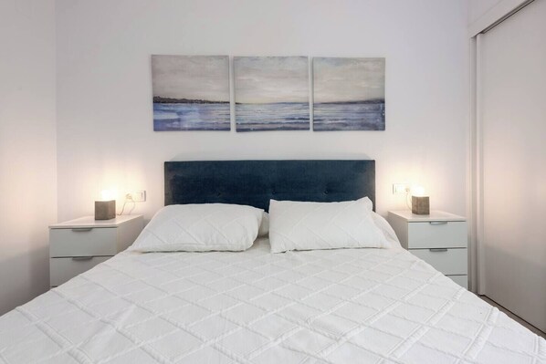 Un dormitorio con una cama grande, dos mesitas de noche y tres cuadros colgados en la pared.