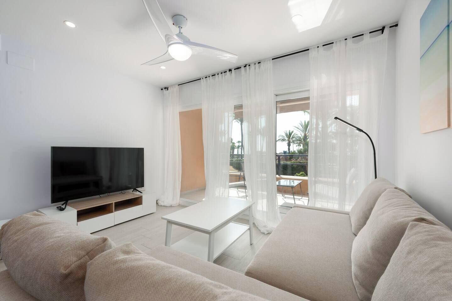 A modern living room with a flat-screen TV, a sofa, a coffee table, and a ceiling fan.