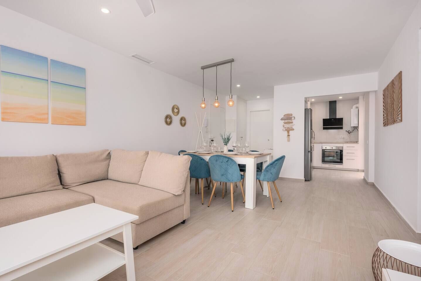 Una sala de estar moderna con un sofá y una mesa de comedor con sillas. Se observa una zona de cocina con electrodomésticos.