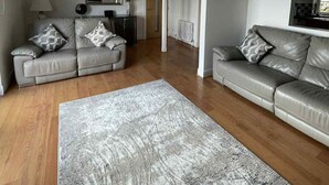 A spacious living room with two grey leather sofas, a large grey rug, and a wooden floor. - Seaview Apartment in Banff (Aberdeenshire)