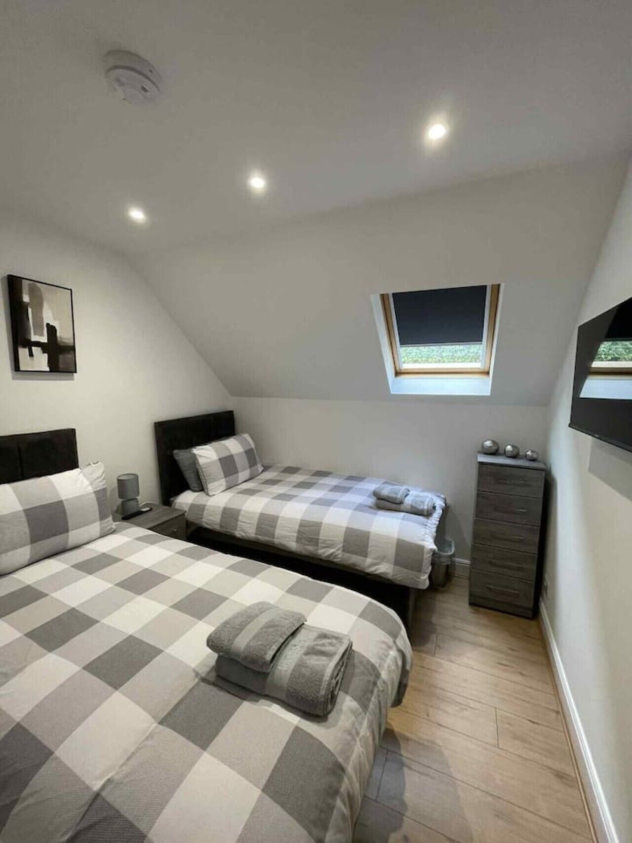 A bedroom with two beds, a window, a ceiling light, and a small cabinet.