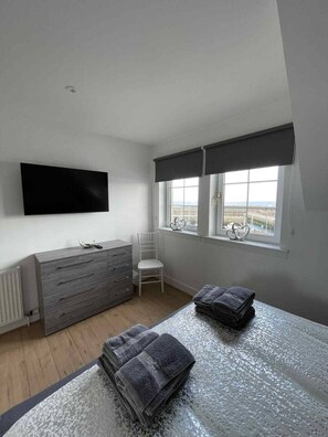 A bedroom with a bed, a dresser, a chair, a window with blinds, and a flat-screen TV mounted on the wall. - Seaview Apartment in Banff (Aberdeenshire)