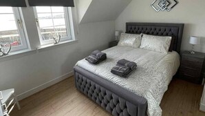 A bedroom with a large bed, a window with blinds, a bedside table, and a wall-mounted light fixture. - Seaview Apartment in Banff (Aberdeenshire)