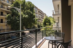Een balkon met een tafel en stoelen, met uitzicht op een straat met gebouwen en bomen.