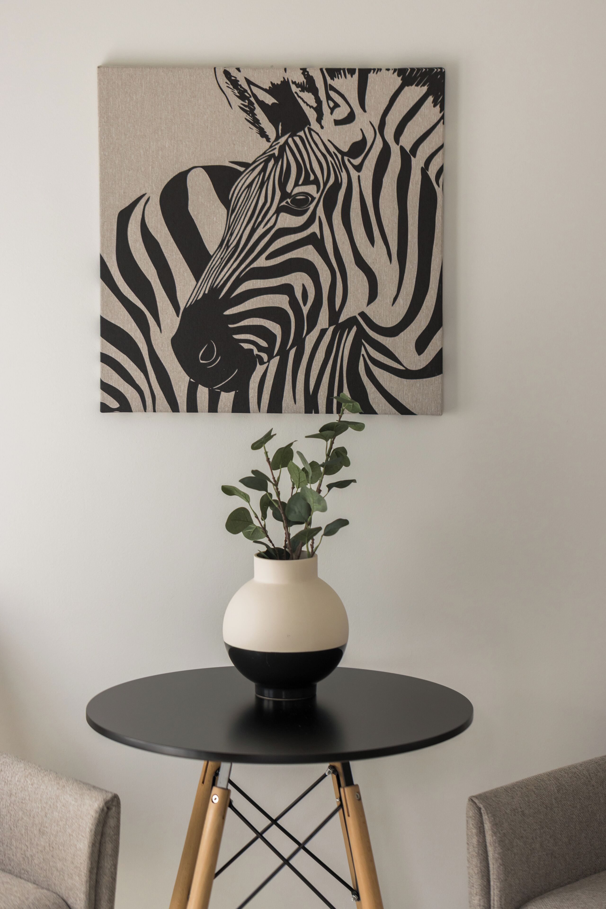 A wall-mounted zebra print artwork above a round table with a vase of green plants.
