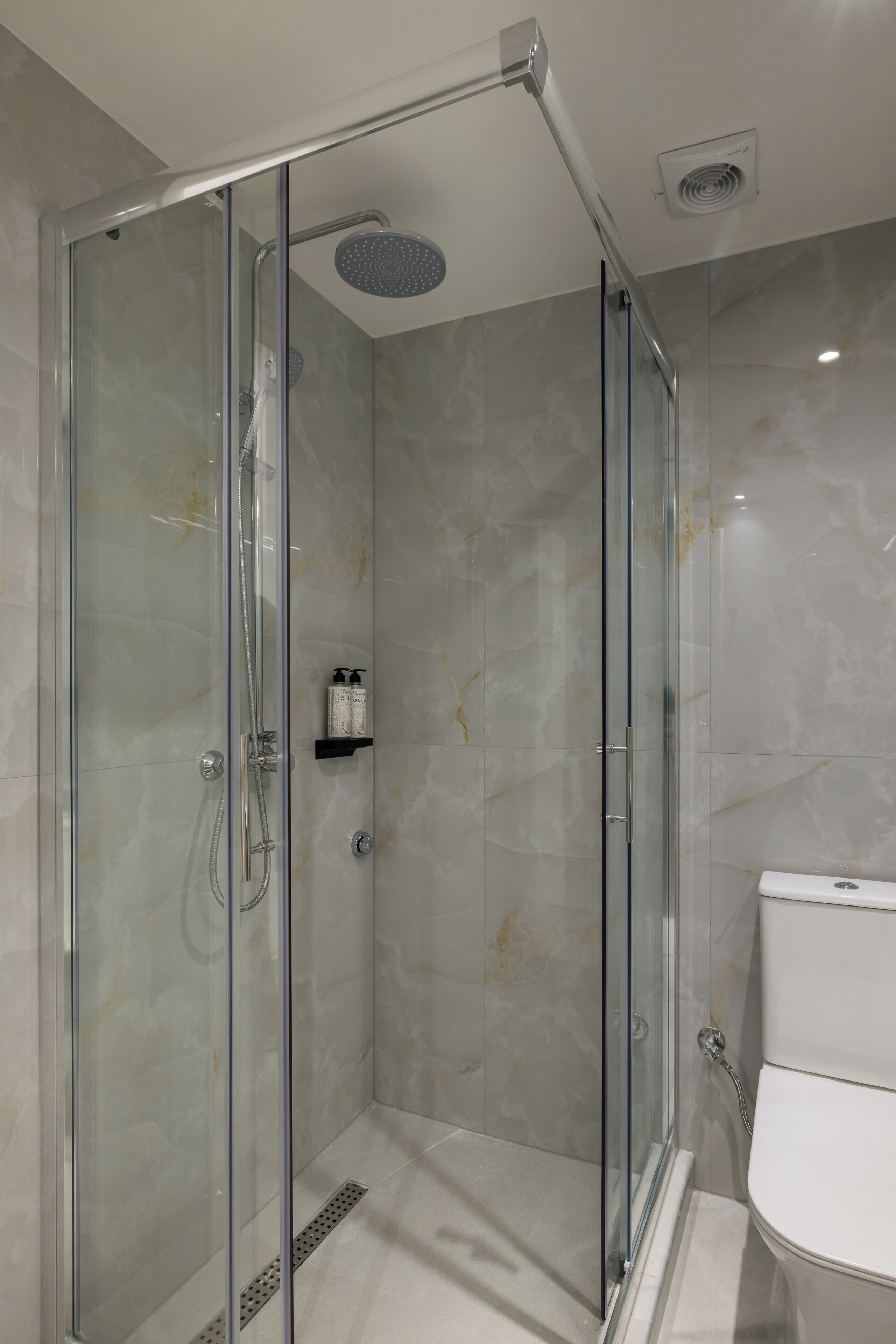 A modern bathroom with a glass-enclosed shower, a toilet, and a marble floor.