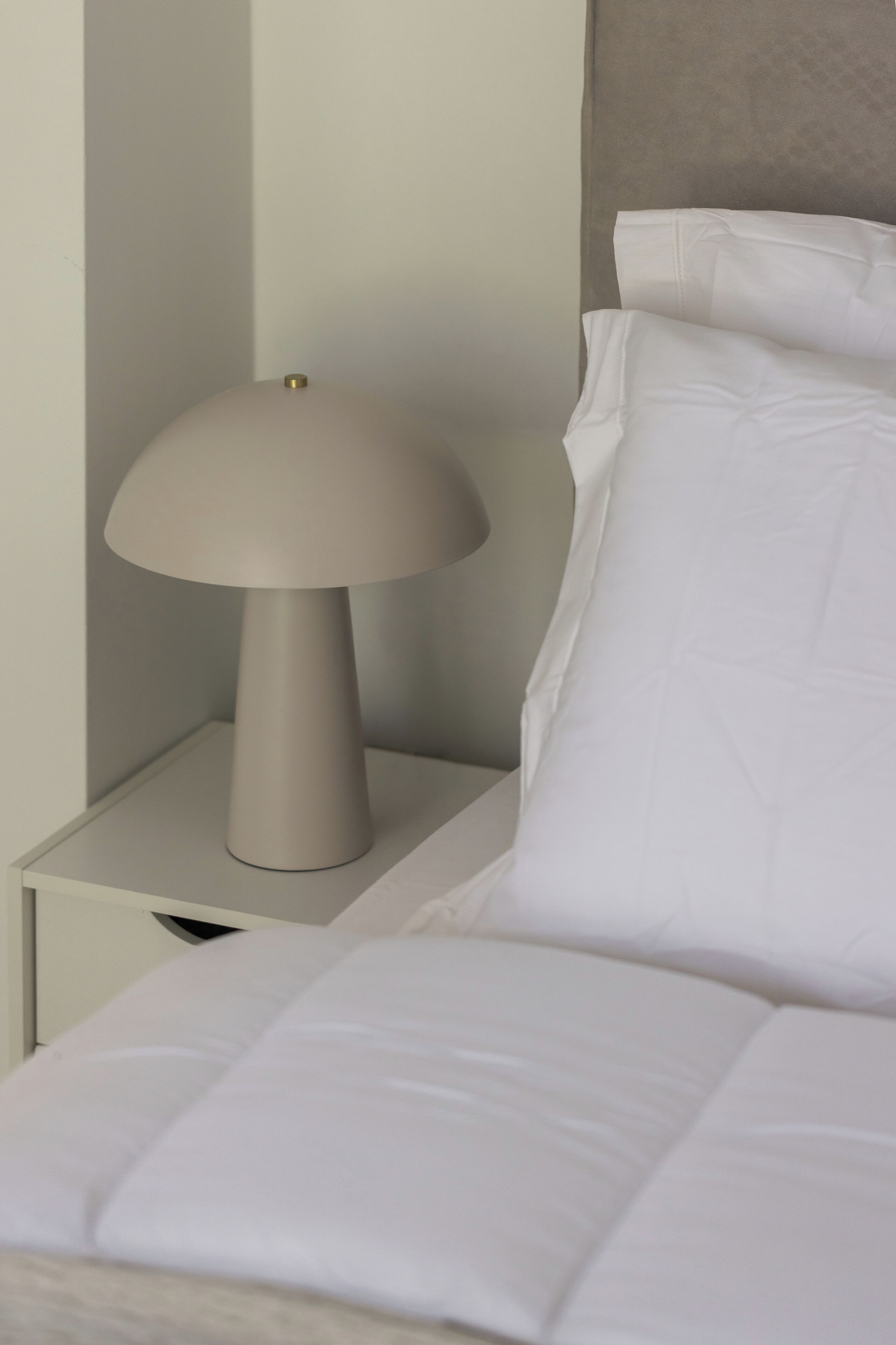 A bed with white bedding and a bedside table with a lamp.