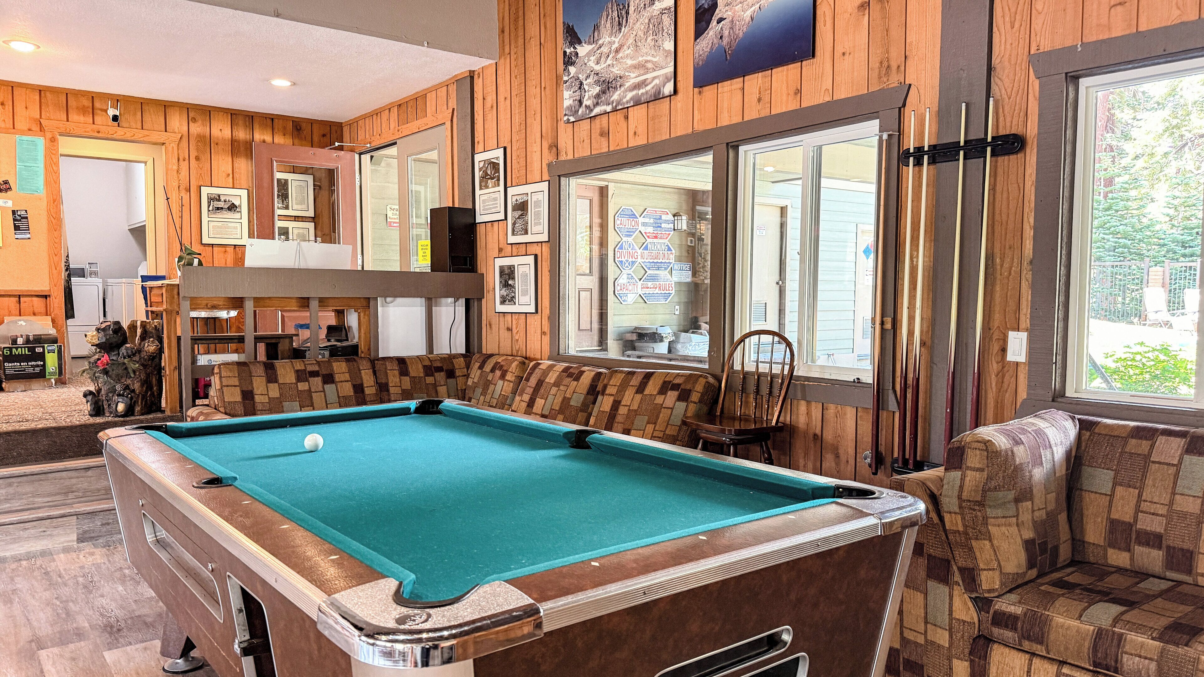 A pool table in a room with wooden paneling, a bench, and a window with safety signs.