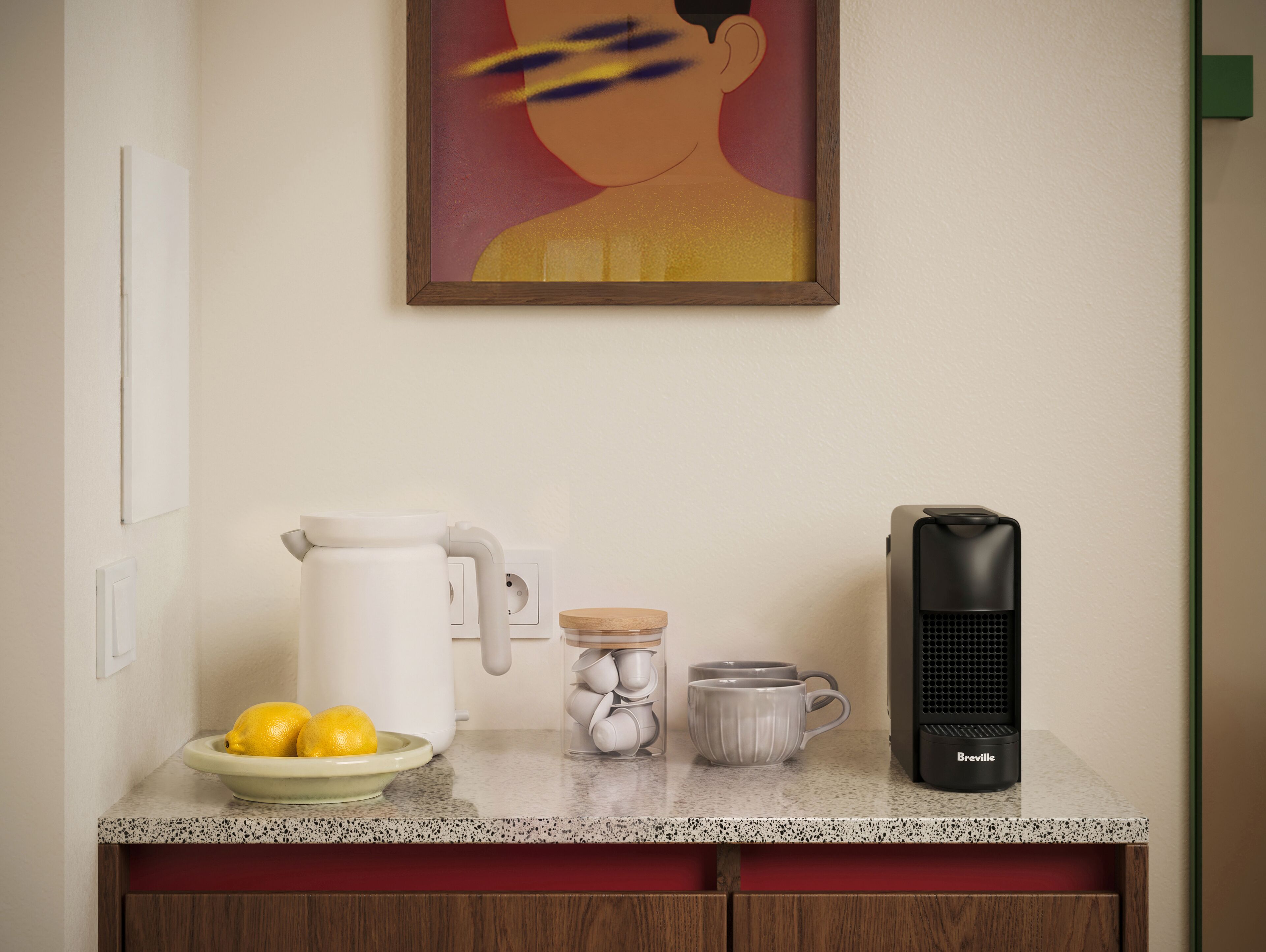 A kitchen counter with a coffee maker, a kettle, a mug, and a bowl of lemons.