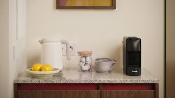 A kitchen counter with a coffee maker, a kettle, a mug, and a bowl of lemons.